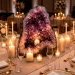 Elegant wedding reception table setting featuring a large amethyst geode centerpiece with soft candlelight and gold tableware.