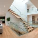 Modern duplex living room featuring a central floating staircase with glass balustrades flooded with bright natural sunlight.