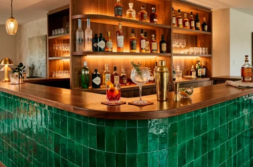 A luxurious home bar featuring a glossy emerald green zellige tiled counter and warm ambient lighting.