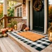 Beautiful fall porch featuring layered black and white plaid rug with a textured autumn doormat and decorative pumpkins.