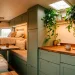 Cozy camper van interior featuring sage green cabinets, warm wood countertops, and hanging plants