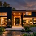 Modern black brick house exterior at twilight with warm cedar wood accents and large glowing windows.