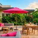 Luxurious sunny backyard patio featuring a gray sofa with bright fuchsia throw pillows and a matching umbrella.