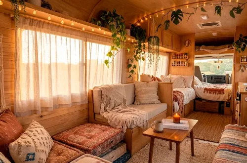 Cozy boho camper van interior featuring plush cushions, macrame decor, trailing plants, and warm string lights at sunset.