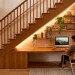 Modern home office built under a wooden staircase with warm lighting and floating shelves.