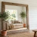 Oversized reclaimed barn wood mirror leaning against a white shiplap wall in a sunlit farmhouse living room.