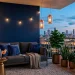 Chic apartment balcony at dusk with navy blue walls, brass accent table, and glowing copper lanterns.