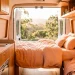 Modern camper van interior decorated with soft peach fuzz bedding and warm wood accents under bright natural light.