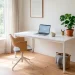 Sleek minimalist white desk in a bright, compact home office featuring a laptop, plant, and soft natural lighting.