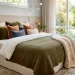 A perfectly layered modern bed featuring linen sheets, a folded white duvet, an olive-green quilt, and a chunky knit throw blanket.