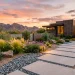 A modern sustainable xeriscape front yard featuring drought-tolerant plants and decorative rocks at sunset.