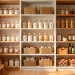 Beautifully organized minimalist kitchen pantry with clear glass jars and bright white shelving.