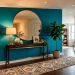 Modern windowless apartment foyer featuring a bold teal accent wall, warm console lighting, and a gold round mirror.