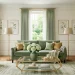 Luxurious living room featuring a sage green velvet sofa, brushed gold floor lamps, and geometric glass coffee table.