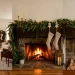 Cozy farmhouse fireplace mantel decorated for the holidays with lush greenery garland, brass candles, and linen stockings.