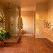 Wide view of a modern sun-baked terracotta bathroom featuring warm clay tiles, matte black fixtures, and lush green plants.
