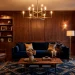Luxurious moody living room with dark walnut paneled walls, navy velvet sofa, and brushed brass chandelier.
