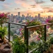 Panoramic view of a lush high-rise balcony garden with vibrant potted plants overlooking a city skyline at sunset