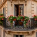 Lush red geraniums spilling from window boxes on a classic French balcony with wrought iron details.