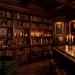 A moody dark academia home bar featuring dark wood bookshelves, crystal decanters, and candlelight