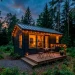 Cozy dark-painted small cabin in a forest with warm string lights and a small deck at twilight