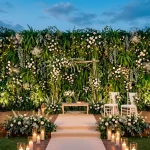 Wide view of an elegant wedding stage featuring a lush greenery wall with ferns and white roses.