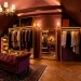 Wide view of a moody plum and gold attic wardrobe featuring velvet seating, brass clothing racks, and warm lighting