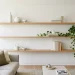 Minimalist living room featuring light oak floating wood shelves with sparse ceramic decor and a trailing plant