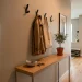 Narrow apartment entryway featuring a slim console table and matte black adhesive wall hooks.