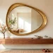 Large asymmetrical brass decorative mirror in a modern entryway above a walnut console table.