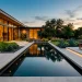 A wide view of a modern minimalist backyard pond with clean concrete edges and calm dark water reflecting the sky.