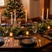 A modern dining table set with matte black plates, gold flatware, and a fresh evergreen runner.