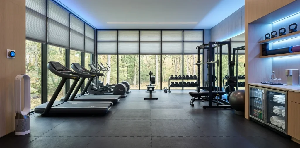 Modern home gym setup with smart thermostat, bladeless fan, and cellular window shades for year-round comfort.