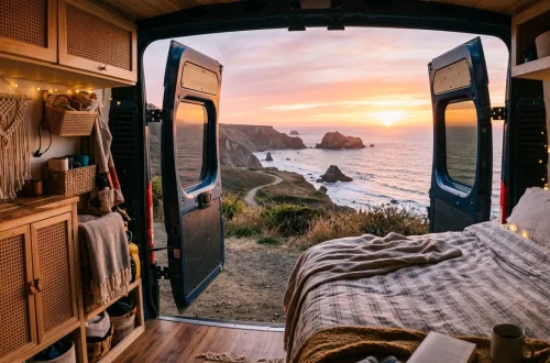 Cozy boho camper van interior with rattan cabinets and wicker baskets facing a coastal sunset