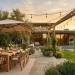 Wide view of a modern backyard patio featuring a large beige cantilever umbrella over a wooden dining set