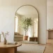 Large arched floor mirror leaning against a wall in a bright modern living room