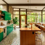 Wide panoramic view of a mid-century modern kitchen featuring emerald green cabinets and warm teak wood accents.