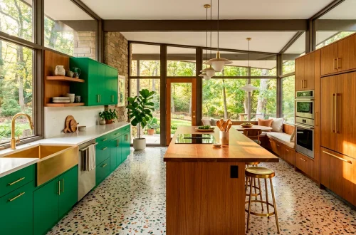 Wide panoramic view of a mid-century modern kitchen featuring emerald green cabinets and warm teak wood accents.