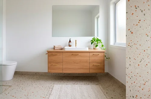 Small modern bathroom featuring large format terrazzo tiles, a floating oak vanity, and brass hardware in a minimalist layout.