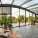 A modern high-tech sunroom with smart glass windows, automated blinds, and lush indoor plants bathed in sunlight