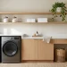 Minimalist laundry room with white washer and dryer under a sleek quartz counter and organized oak floating shelves.