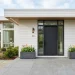 A modern minimalist front porch featuring clean lines, a sleek charcoal door, and geometric planters with spring flowers.