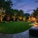 Beautiful modern backyard at dusk with warm uplighting illuminating large trees
