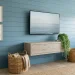 Serene coastal blue bedroom featuring a wall mounted TV above a floating light oak console with rattan accents.