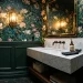 Dark green powder room with bold floral wallpaper and a marble vanity under warm brass lighting.
