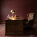 Moody home office featuring deep burgundy walls, a vintage walnut desk, and a tufted brown leather chair