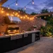 Wide view of a stunning industrial style backyard kitchen featuring exposed brick and stainless steel grill