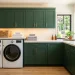 Stunning small modern laundry room renovation featuring a stacked washer, green cabinets, and warm ambient lighting.