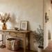 Earthy Mediterranean foyer with terracotta floor tiles, a rustic wooden console, and limewashed walls catching warm sunlight.