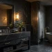 Luxurious moody dark bathroom interior featuring black marble vanity and raw slate accent wall with warm brass lighting.